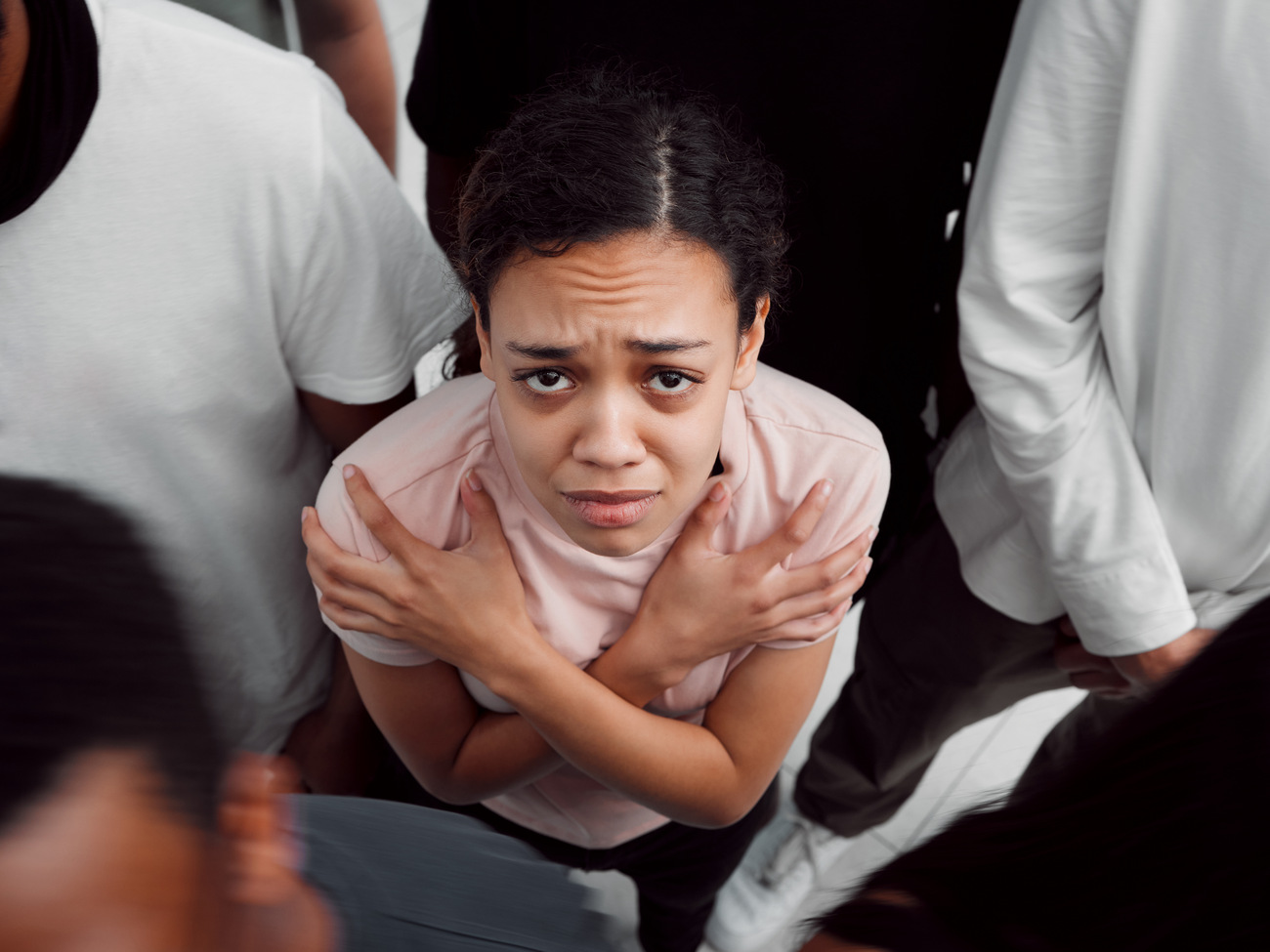Eine junge Frau mit verschränkten Armen wirkt ängstlich und unsicher in einer belebten Menschenmenge.