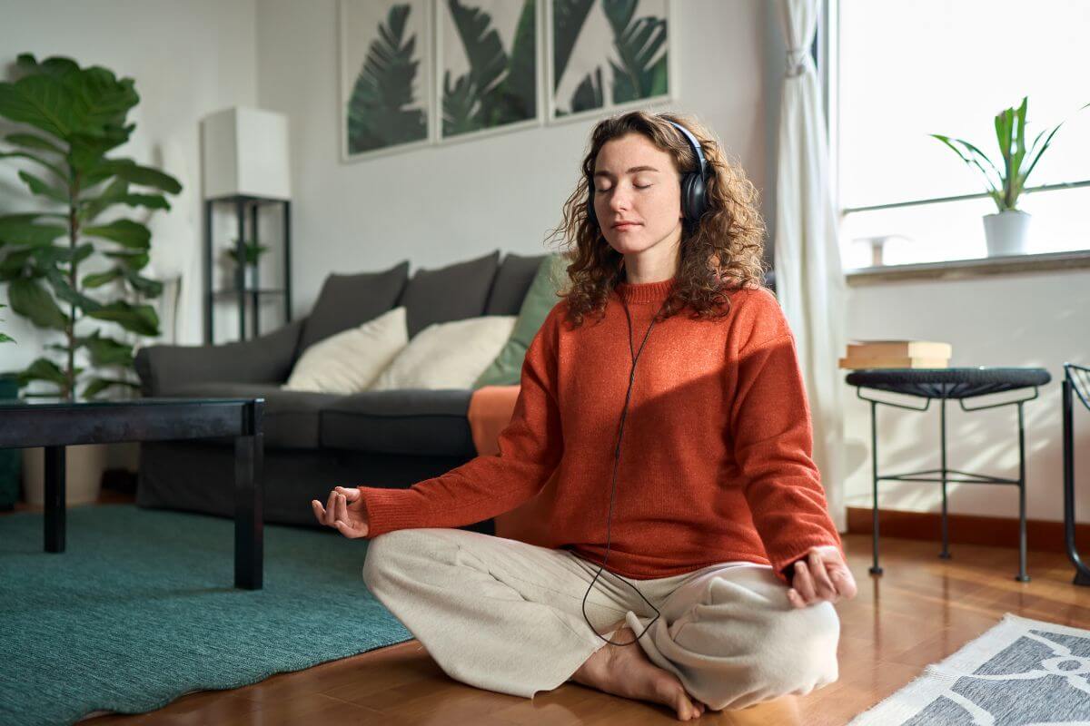Frau macht Yoga zu Hause und trägt dabei Kopfhörer.