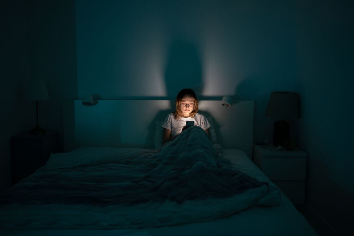 Eine Frau sitzt nachts im Bett und schaut konzentriert auf ihr Handy.