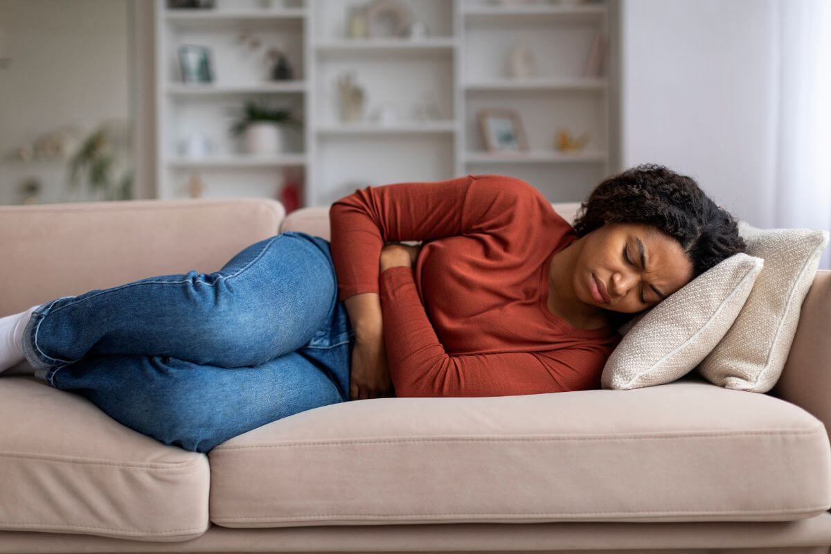Eine Frau liegt auf der Couch und hält sich den Bauch, sichtbar von Magenproblemen betroffen.