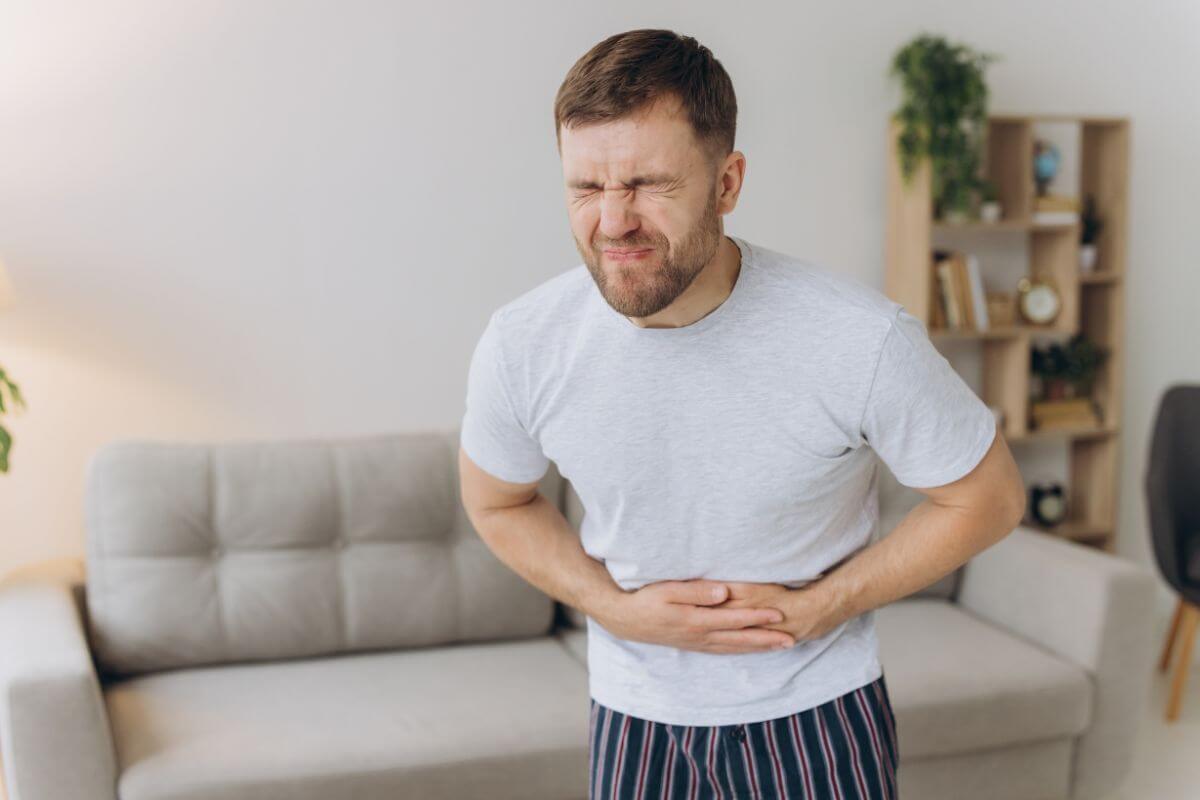 Ein Mann hält sich schmerzhaft den Bauch und zeigt Symptome von Magenproblemen.
