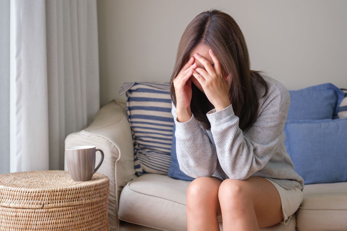 Frau sitzt auf Sofa mit den Händen im Gesicht – innere Überforderung als Stressreaktion