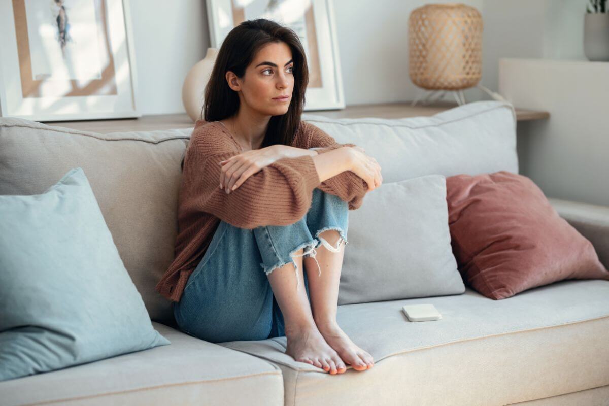 Frau sitzt nachdenklich auf dem Sofa – innere Unruhe und Grübeln als typische Symptome einer Angststörung.