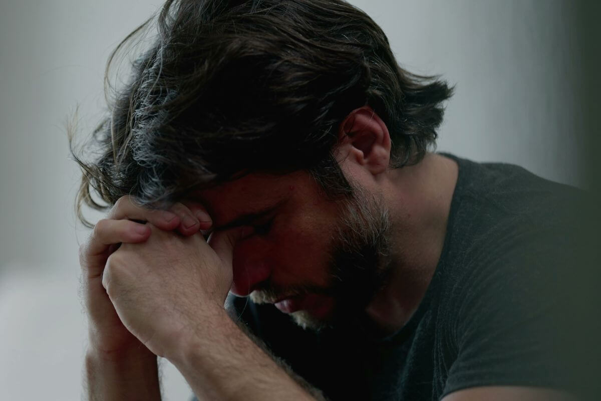 Nachdenklicher Mann mit gesenktem Kopf und Anspannung in den Händen – dargestellt als Belastung durch Angst oder innere Unruhe.