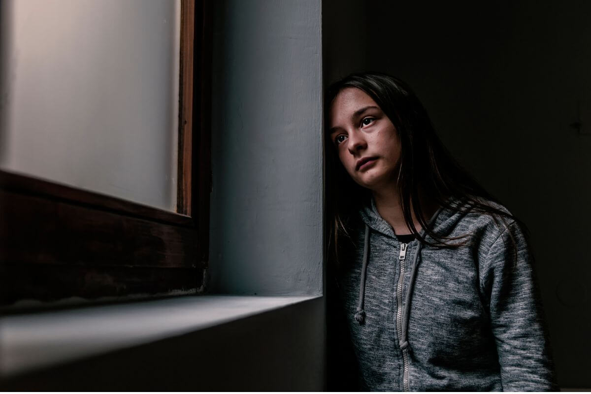 Junge Frau schaut nachdenklich aus dem Fenster – dargestellte innere Belastung und Unsicherheit, ob psychotherapeutische Hilfe benötigt wird.