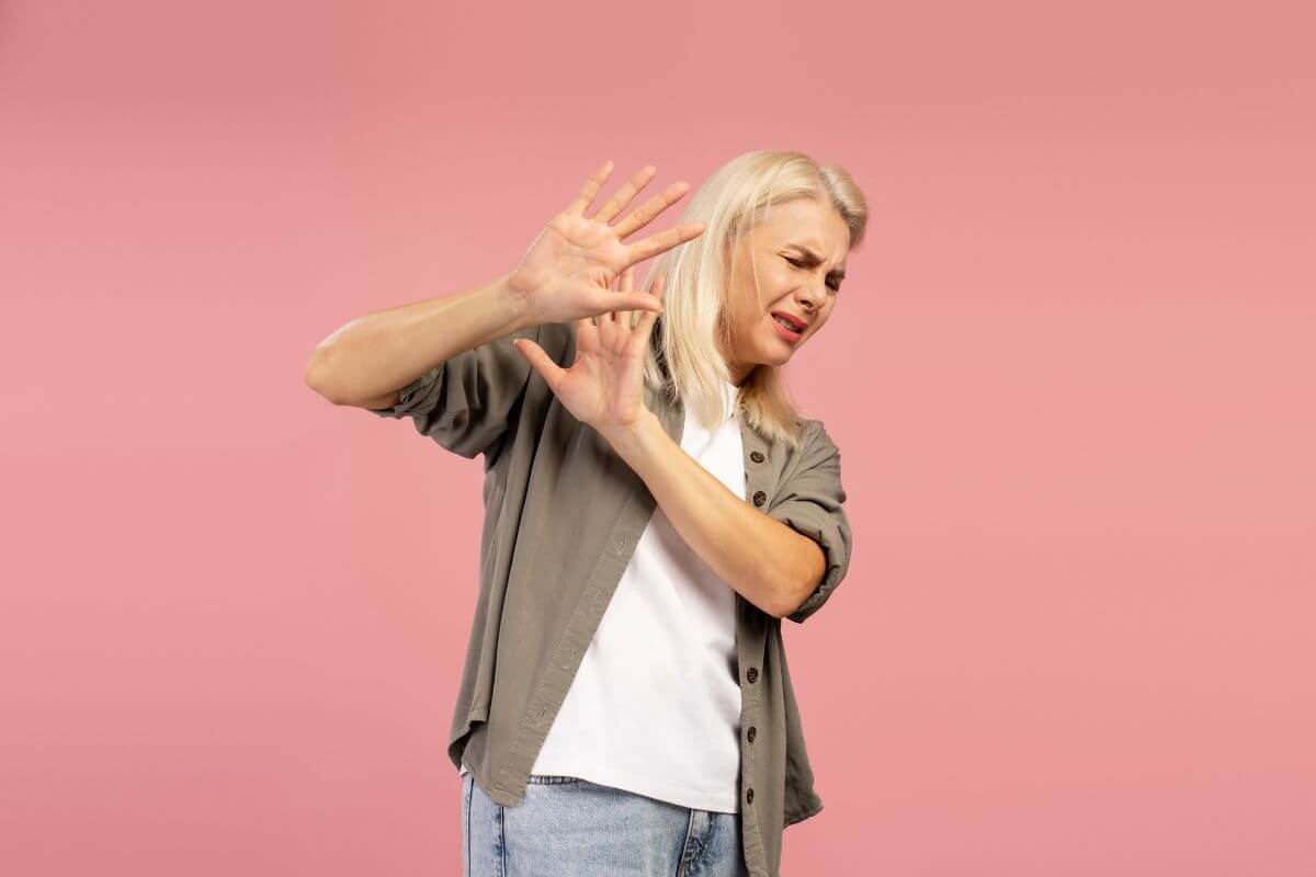 Frau mit Abwehrhaltung vor rosa Hintergrund – zeigt eine typische Reaktion bei Angst und Vermeidungsverhalten.