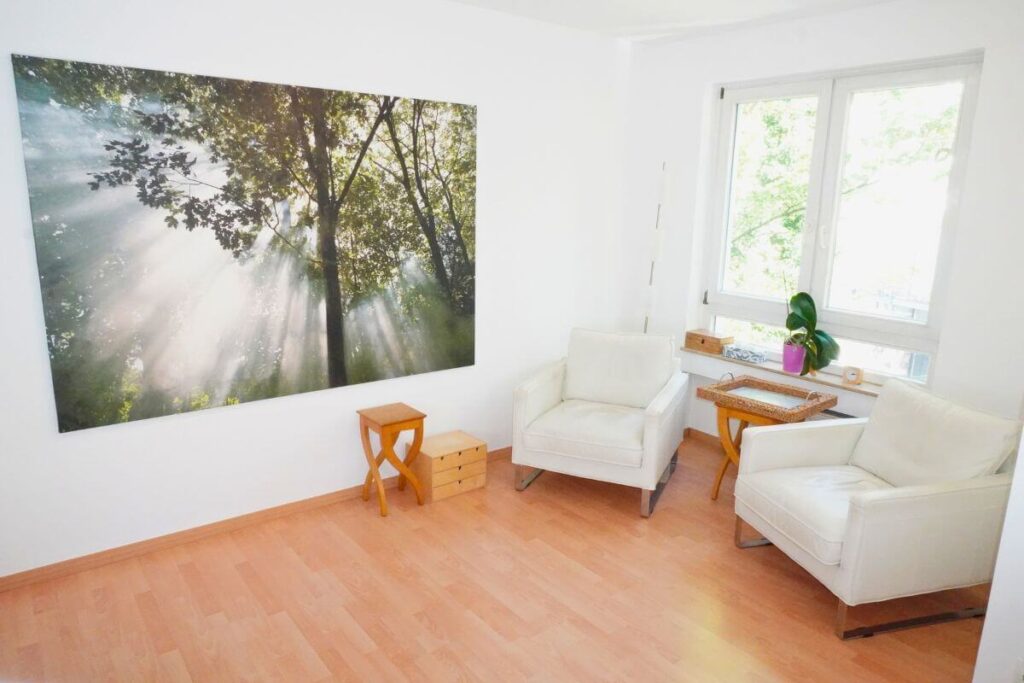 Heller Praxisraum von Oliver Hox in Köln mit zwei Sesseln und beruhigender Waldfotografie an der Wand – angenehme Atmosphäre für Gespräche bei Panikattacken.